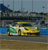 Pixelated static image shows a yellow vehicle with green accents on a brown surface, blue water, and a gray background with vertical lines.