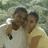 Two figures in close embrace, one in white shirt, one in light brown shirt, against blurred green background with white highlights.
