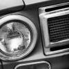 Black-and-white close-up of a vehicle's headlight and grille section with circular headlight and mesh grille pattern.