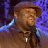 Pixelated static image of a person wearing a brown hat and dark clothing against a purple background with blue light effects.