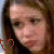 Pixelated close-up of a person with light skin tone, brown hair, and dark eyes; red heart outline in bottom-left corner.