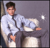 A person in a light blue shirt and dark tie sits on a white fur chair against a gray background with a starburst graphic.