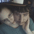 A pixelated image of a person with dark hair wearing a dark hat and blue clothing, resting their head on their hand with a neutral expression.