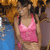 A woman in a pink tank top and blue jeans stands against a blurred background with orange and brown tones.