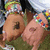 A cartoon character with brown skin and colorful beaded bracelets lies on grass, head turned left, eyes closed, wearing a white top with black trim.