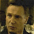 Pixelated close-up of a person's face with light skin tone, dark hair, and neutral expression against a dark background.