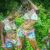 A pixelated image of a person in light-colored crop top and denim shorts standing against green foliage background.