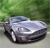 Pixelated silver car with dark wheels on a light surface, green foliage background, static image.