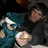 Two figures in dark clothing hold a smaller figure wearing teal and white; the rightmost figure's head shifts slightly left to right.