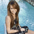 A woman with long brown hair sits holding a black object against a blue water background.
