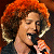 A pixelated contact sheet showing two frames of an animated icon featuring a person with curly red hair singing into a microphone on the left and green text reading "Original Icons .com" on the right against a dark background.