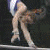 A gymnast in a white leotard performs on a balance beam with another athlete visible behind her.