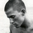 Black-and-white photo of a person with short hair resting their chin on a hand, next to pixelated text reading "He Is Definitely...... THE MAN" on blue background.