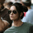 A pixelated static image shows a person with dark hair wearing sunglasses and a light green top against a blurred background.
