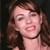 Pixelated close-up of a person with brown hair and light skin, mouth open showing teeth, dark background, static image.