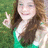 A pixelated image shows a person with long brown hair wearing a green top, making a peace sign with their right hand against a blurred green background.
