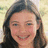 Pixelated close-up of a person with long dark hair smiling, light background.