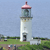 A static pixelated image of a white lighthouse with a pink and maroon top, set against a light blue sky and green grassy terrain.