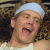 A person wearing a light blue headband and white tank top lies on a patterned surface with mouth open, overlaid by red text reading "MALIBU" above black text "ghost wanted."