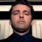 Pixelated close-up of a person with closed eyes, dark hair, and a dark blue shirt against a light and dark striped background.