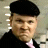 Pixelated portrait of a person wearing a black beret and dark jacket with a light-colored shirt underneath against a muted background.