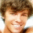 Pixelated close-up of a person with brown hair and light skin smiling, showing teeth against a bright background.