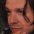 Static pixelated image of a person's face with visible facial features and partial hair, rendered in warm tones on a dark background.