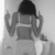 A grayscale image of a person with long dark hair viewed from behind, wearing a sleeveless top with horizontal stripes, making a gesture with both hands raised near the head.