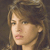 Pixelated close-up of a person with light brown hair and fair skin, showing partial facial features against a dark background.