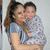 Woman holding child in light blue shirt with patterned blanket, both smiling against plain background.