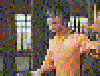 A shirtless man in a prison with barred windows performs a sequence of arm movements including raising, extending, and crossing arms