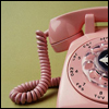 A close-up of a pink rotary telephone with a coiled cord against a muted green background.