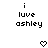 Black pixelated text 'i luve ashley' on white background with two heart symbols below, one static and one animated.