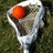 A static image of a lacrosse stick with an orange ball in the net, overlaid with text labels.