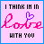 Static pixel art icon with pink background and blue border displaying text "I THINK IM IN LOVE WITH YOU" where the 'O' in LOVE is a purple heart symbol, rendered in blocky black text above and below stylized pink cursive letters.