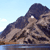Pixelated mountain scene with dark blue peak, brown and gray slopes, light blue sky, and water reflection below.