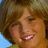 Pixelated image of a person with light brown hair smiling, set against red background with black pixel-art borders.