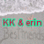Static pixel art displays red text 'KK & erin' with green outlines on a gray background, featuring visible digital noise and low-resolution rendering.