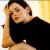 Pixelated image of a person with light brown hair wearing a black top, resting their head on a light-colored surface against a gradient background.