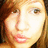 Pixelated close-up of a person's face with light skin, brown hair, and pink lips, showing a slight smile.