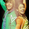 Two people stand side-by-side with arms raised, wearing colorful clothing and smiling, with a white heart outline on the left person's shirt.