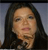 Pixelated close-up of a person with long dark hair against a gradient background, showing facial features and partial neck.