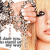 A close-up of a person with blonde hair holding a large silver chain, with text reading 'I dare you to stand in my way' below the chain.