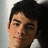 Pixelated close-up of a person with dark hair and light skin, wearing a white shirt against a light background.