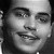Black-and-white pixelated close-up of a smiling person's face with visible eyes, nose, mouth, and dark hair on the left side.
