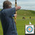 Pixelated image of a person in dark clothing holding a bow and arrow, aiming at a circular target with concentric colored rings on a grassy field.