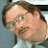 Pixelated close-up of a person with light skin, brown hair, and a mustache wearing a light-colored shirt against a blurred background.