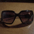 A static image shows dark sunglasses on a brown surface, with text and symbols to the right.