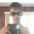 Pixelated image of a person with dark hair wearing sunglasses and holding an object near their face against a blurred background.
