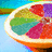 A sliced citrus fruit with segmented colored flesh in red, green, yellow, and purple hues against a blue background.